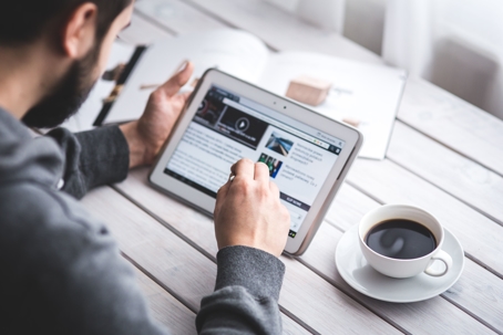 person reading news on tablet next to coffee cup on desk